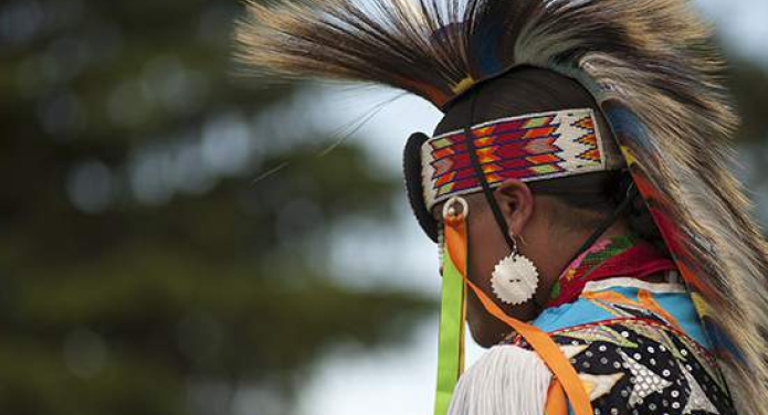 A Native American Man facing away from the camera showing his roach and beaded headpiece.