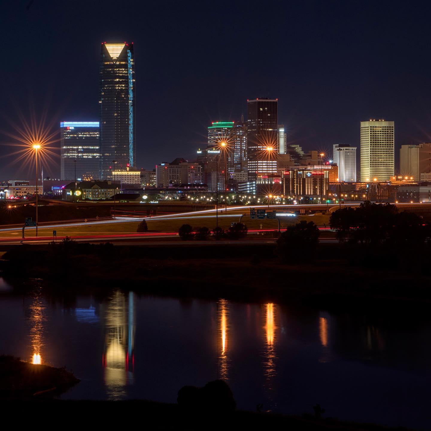 The Oklahoma City skyline at nighttime with the lights reflected in the Oklahoma river.