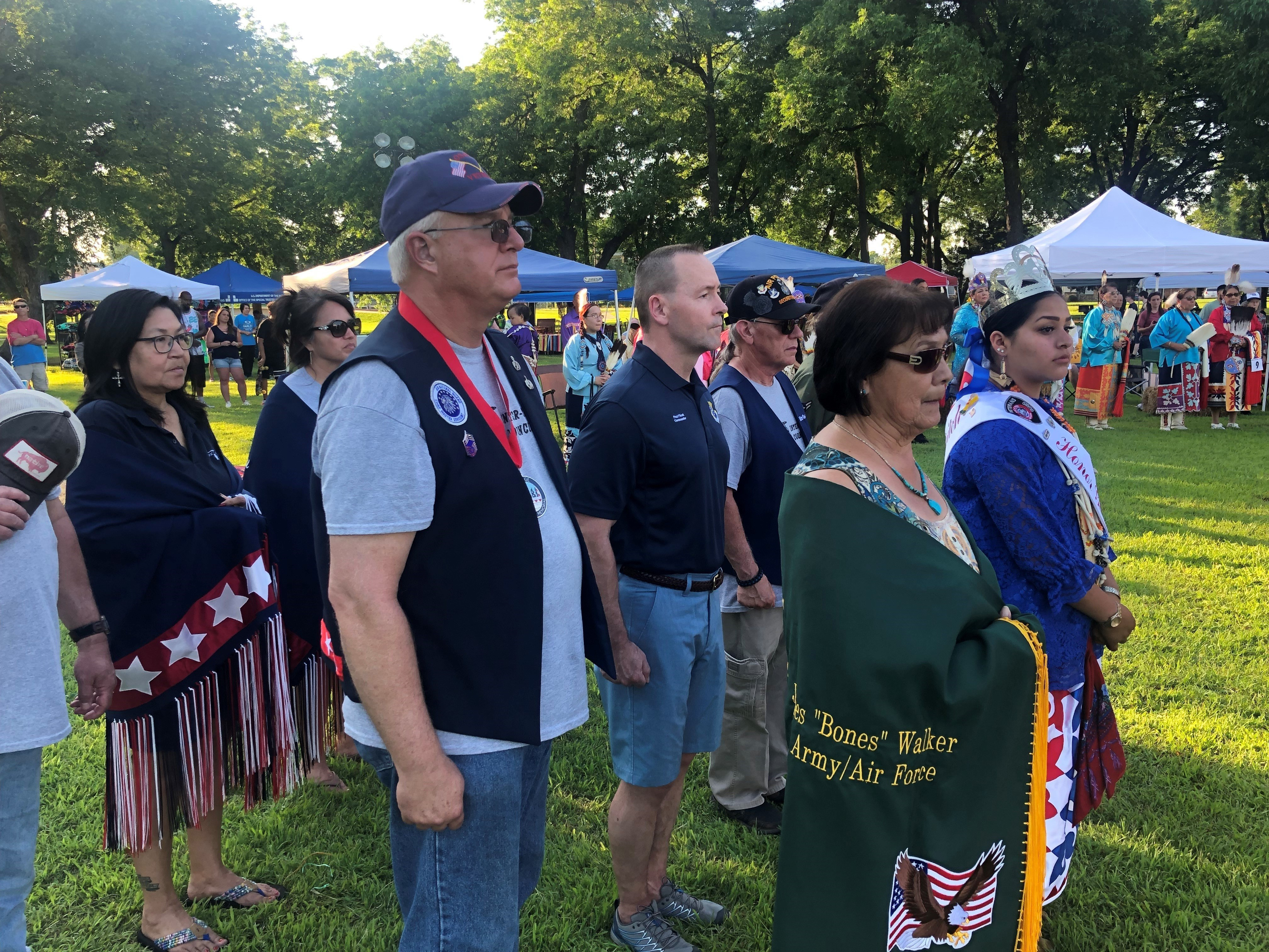 Several men and women facing forward in a procession at a powwow arena.