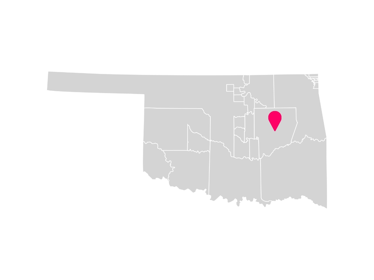 A gray map showing the tribal jurisdiction areas of Oklahoma with a pink pin marking Okmulgee, Oklahoma, where the Muscogee (Creek) Nation is headquartered.