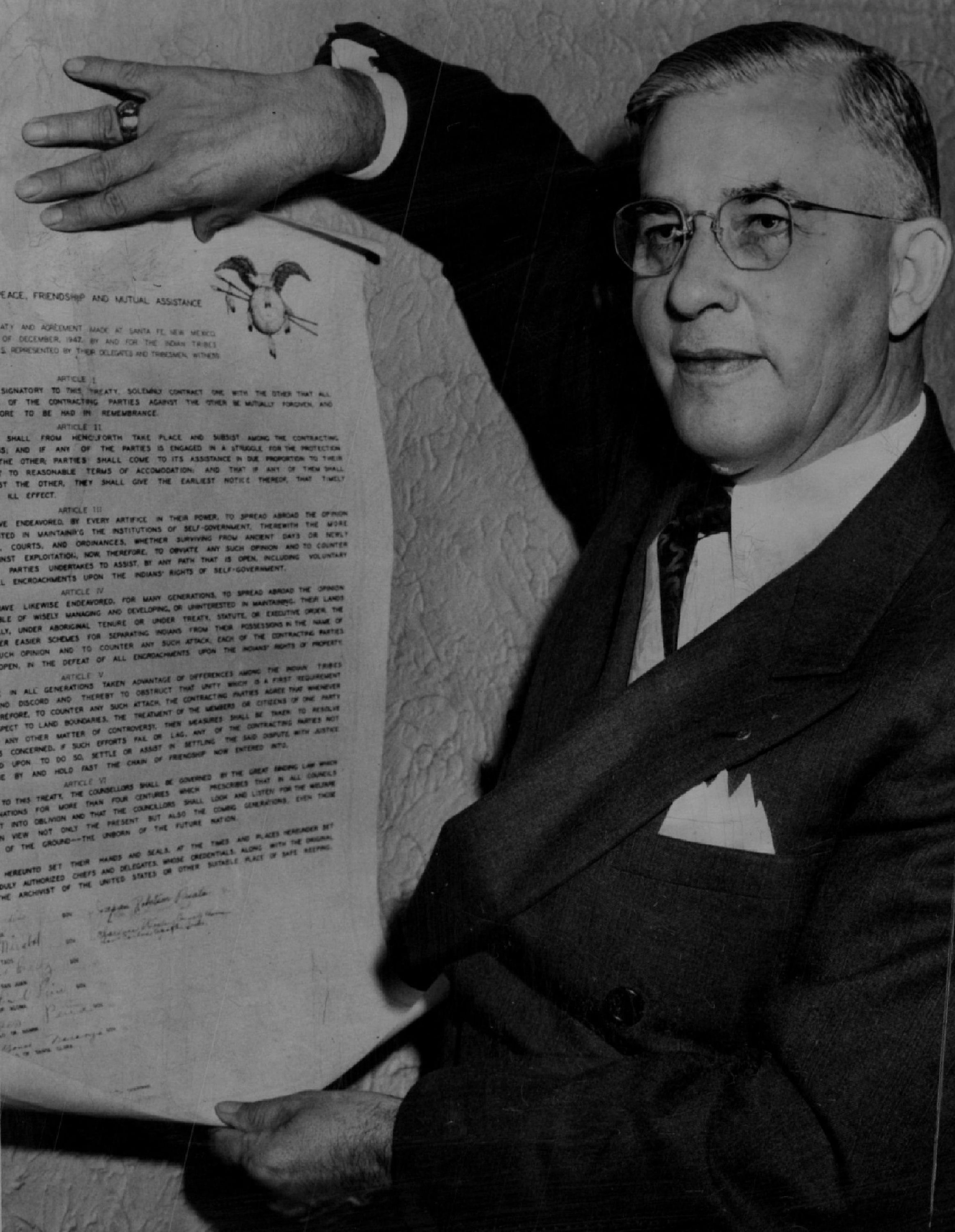 A black and white photograph of a man holding a document upright.