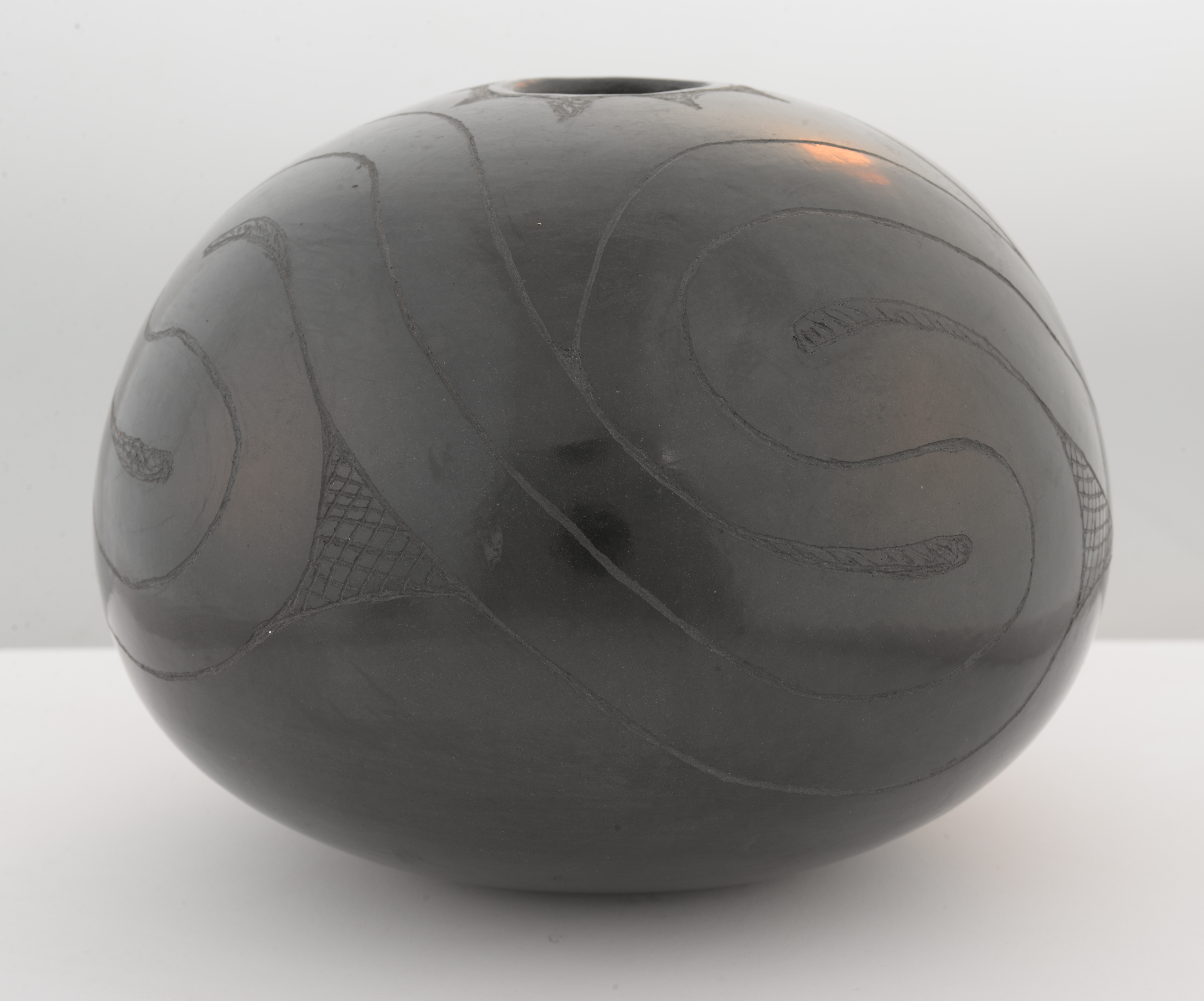 Small ceramic vessel with incised designs on a blank background.