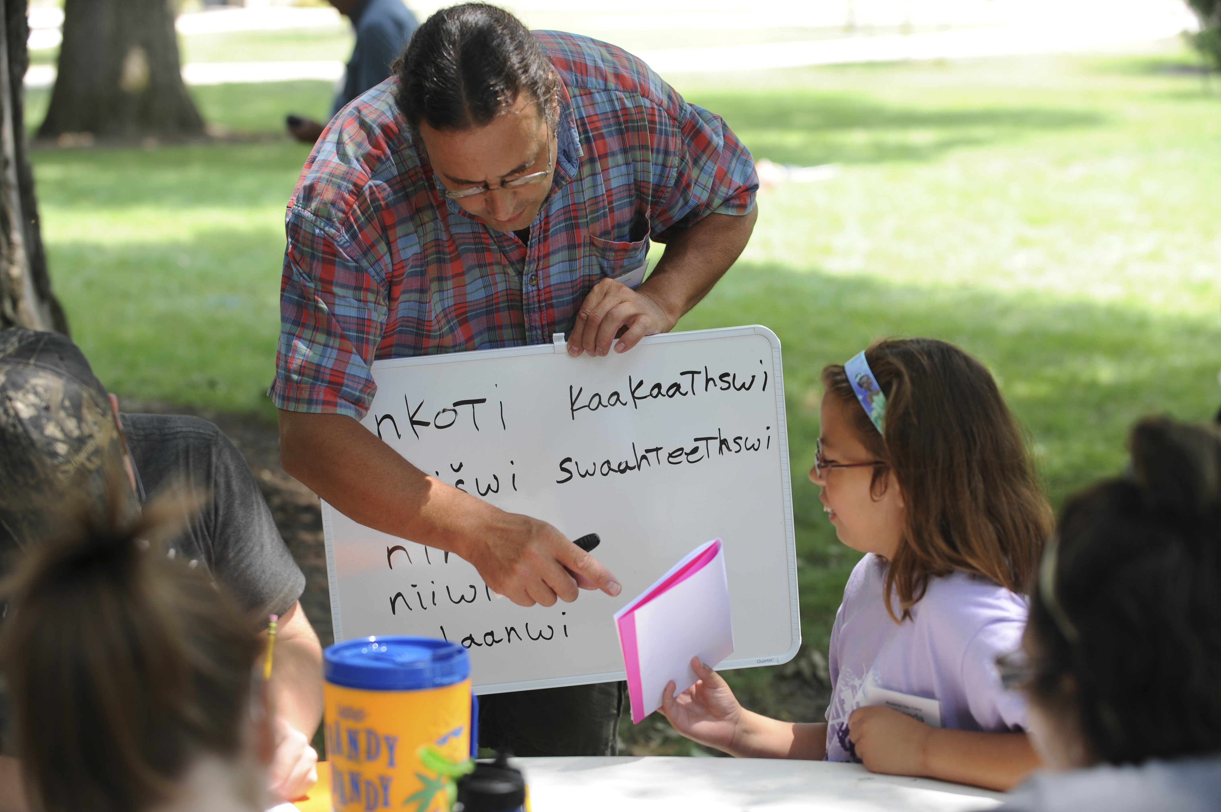 A man holding a whiteboard in front of several children seated at a table.