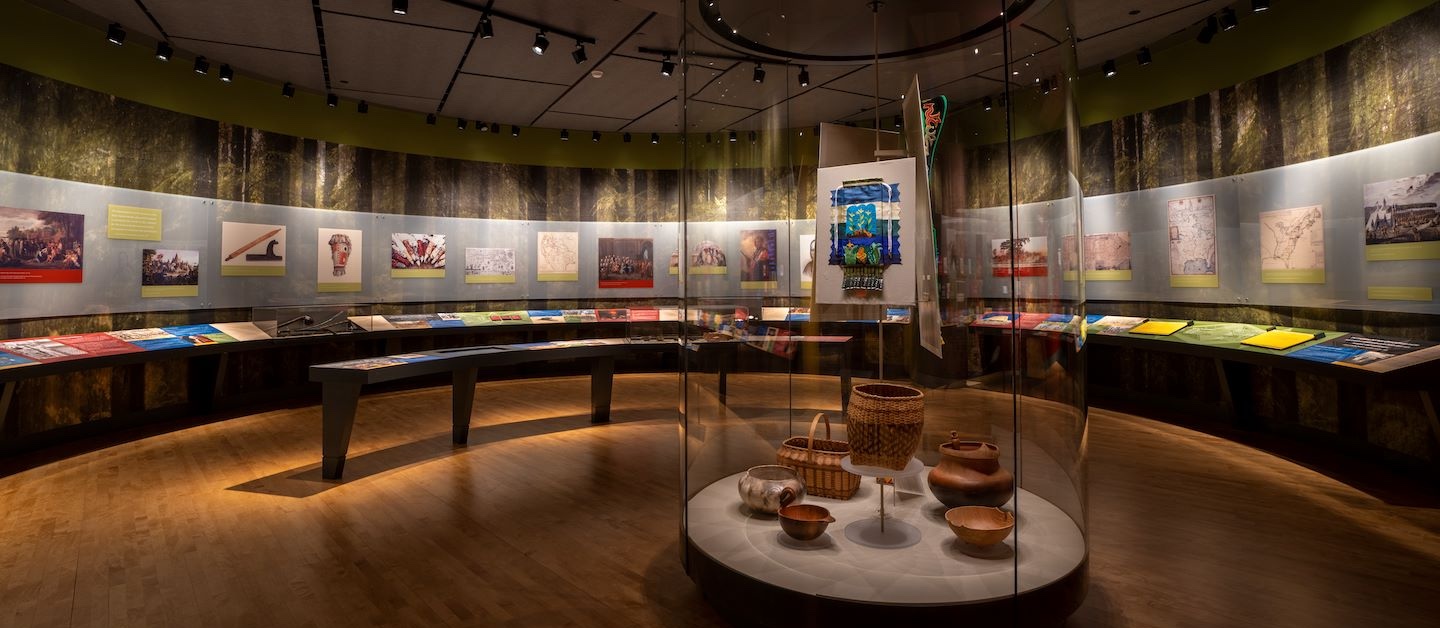 Inside of the "Ancient Roots" section of the OKLA HOMMA exhibit at First Americans Museum showing artist recreations of traditional basketry and historical paintings and photographs of Native American history.